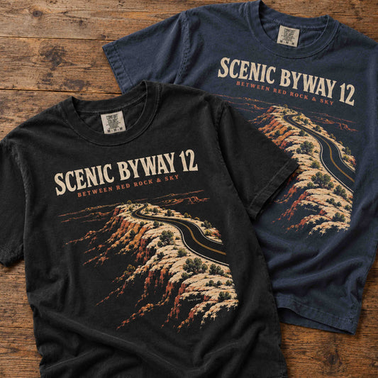 Black and navy Scenic Byway 12 T-shirts laid flat, showing the Utah red rock road design and Between Red Rock & Sky lettering.