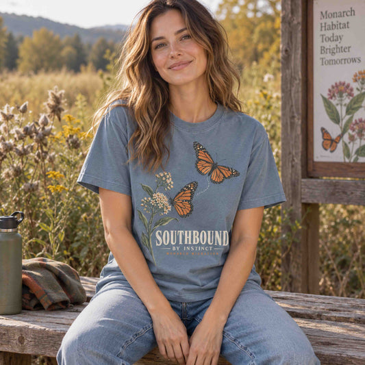 Woman seated on a wooden bench wearing a Blue Jean Southbound by Instinct monarch butterfly graphic T-shirt.