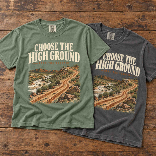 Choose the High Ground graphic tees in Moss and Pepper layered on a wooden table, showing the desert trail print.