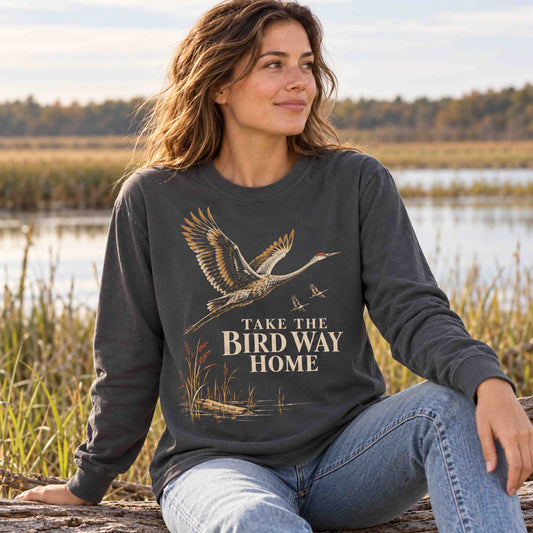 Woman seated by a wetland wearing the Pepper sandhill crane long sleeve shirt.