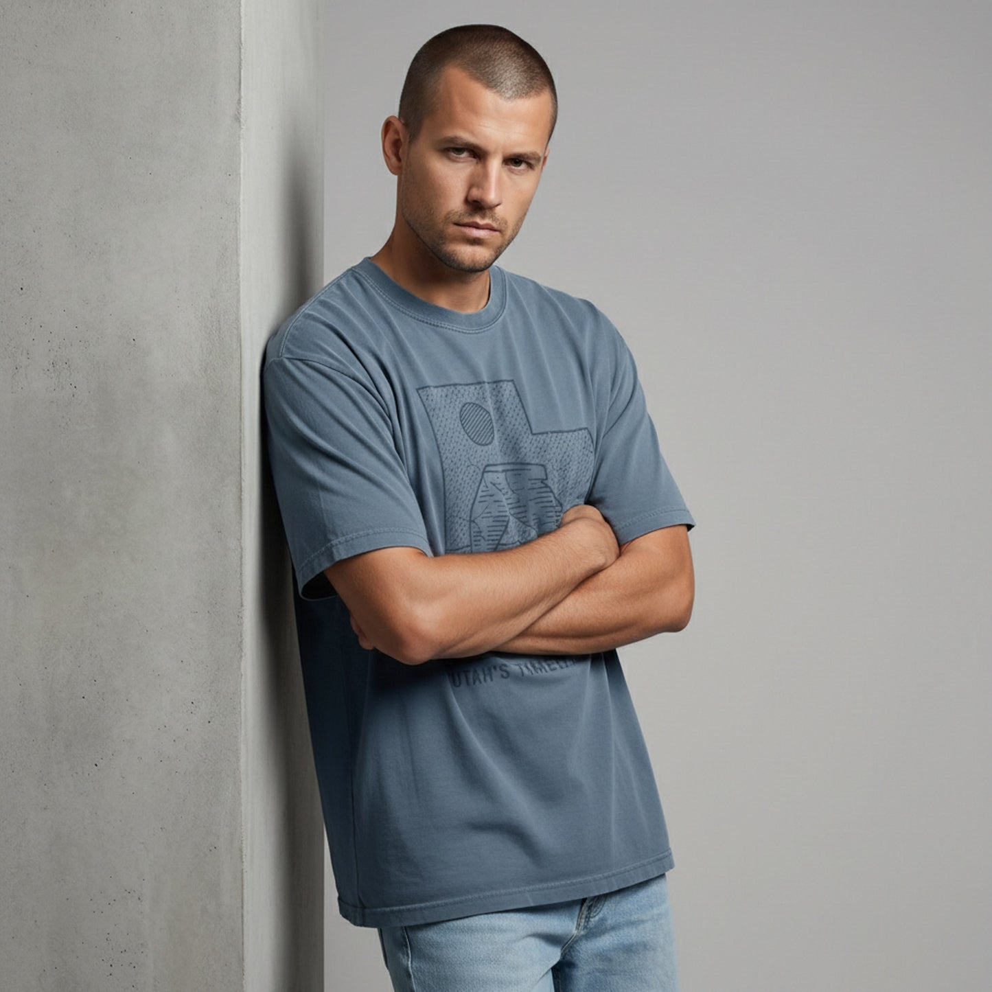 Front view of a man with arms crossed, wearing a dusty blue outdoor lifestyle t-shirt with a vintage national park graphic.