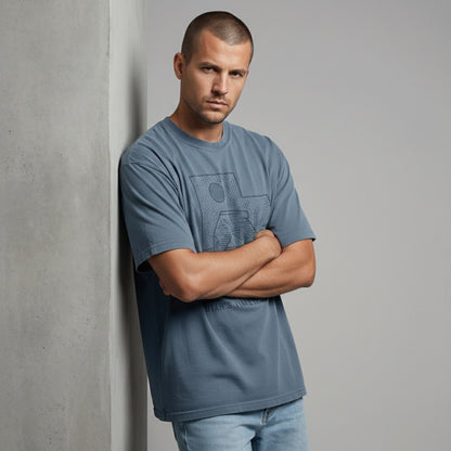 Front view of a man with arms crossed, wearing a dusty blue outdoor lifestyle t-shirt with a vintage national park graphic.