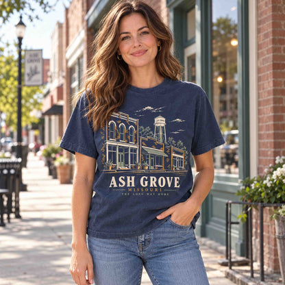 Woman wearing a Navy Ash Grove Missouri graphic T-shirt on a sidewalk lined with brick storefronts.
