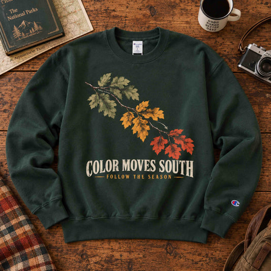 Being is Good Color Moves South sweatshirt in Dark Green, laid flat on a wooden table with autumn leaves artwork.