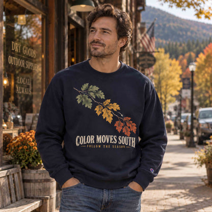 Man wearing a Navy Being is Good Color Moves South sweatshirt on a small-town street with fall foliage.