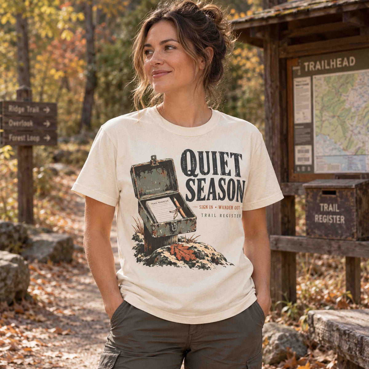 Woman wearing an Ivory Quiet Season Trail Register graphic tee in a fall hiking setting