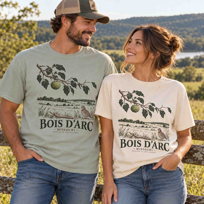 Man and woman wearing Being is Good Bois D'Arc Missouri T-shirts in Bay and Ivory, featuring Osage orange and bobwhite quail artwork.