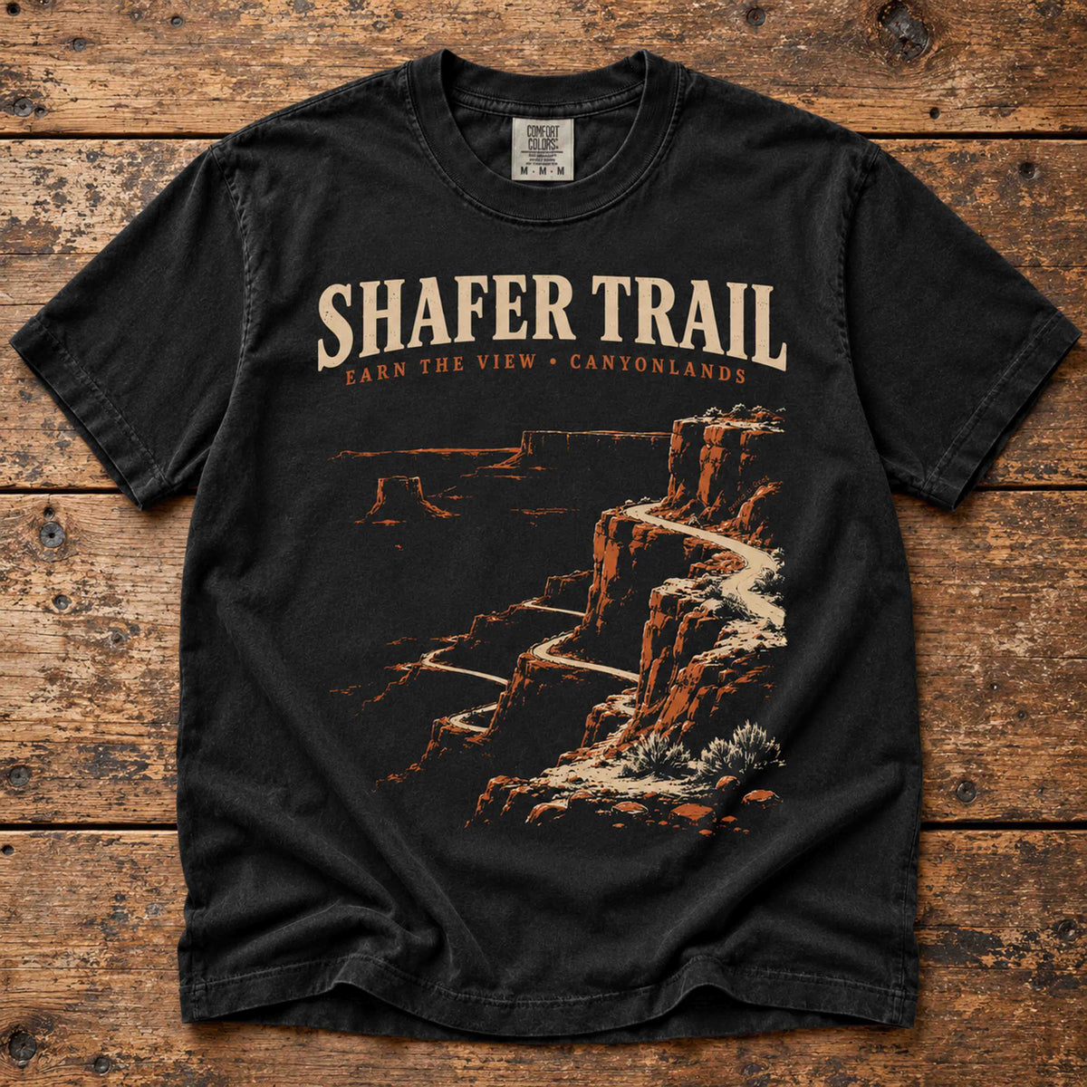 Overhead view of a Black Shafer Trail Canyonlands T-shirt with winding canyon road artwork.