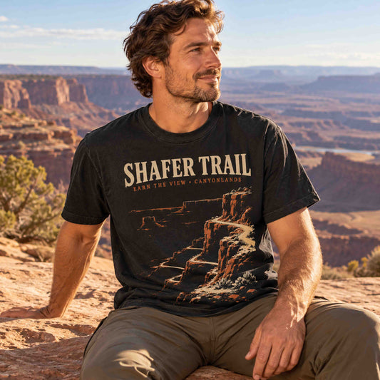 Man wearing a Black Shafer Trail Canyonlands graphic T-shirt while seated at a Utah canyon overlook.
