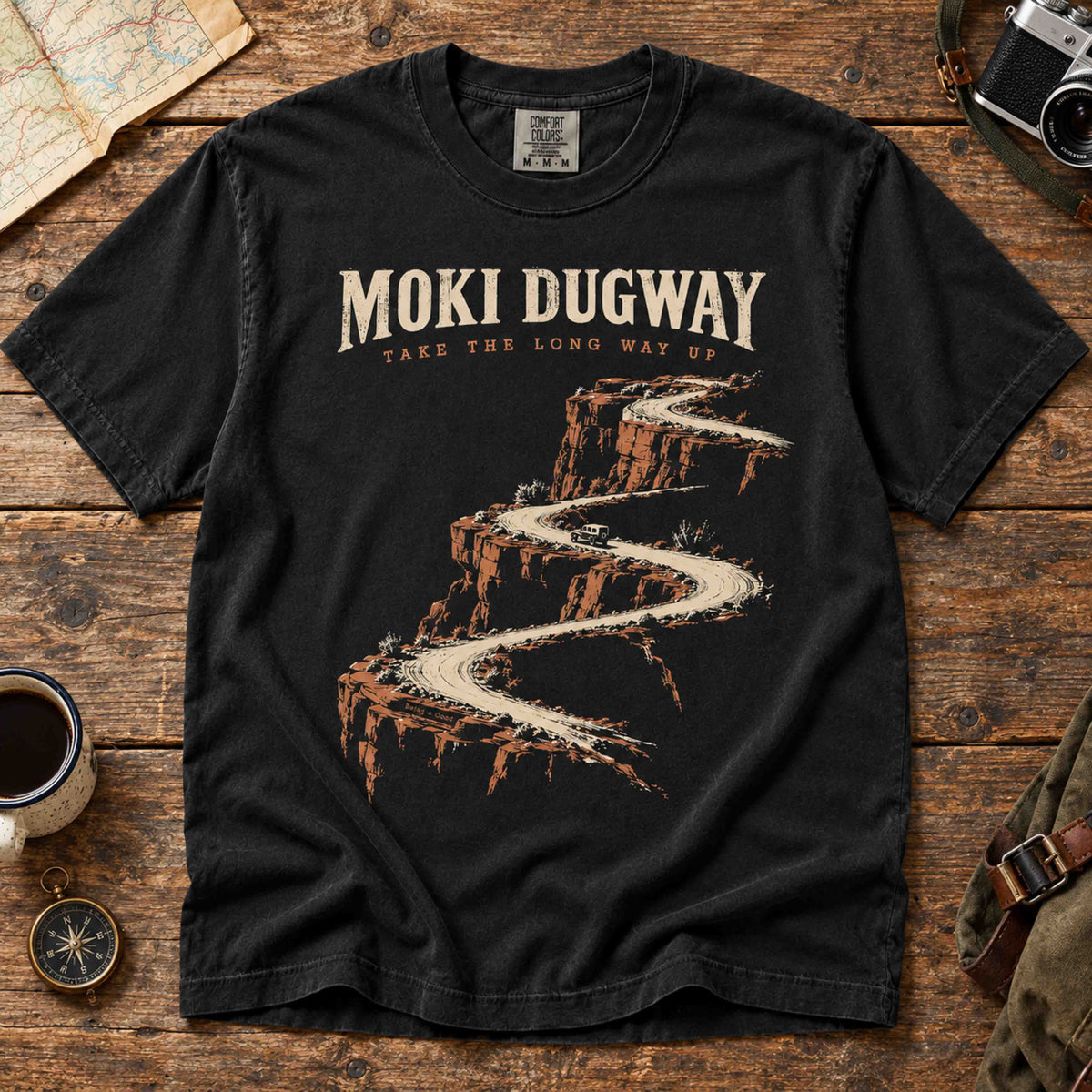 Overhead view of a Black Moki Dugway Utah T-shirt with winding desert road artwork.