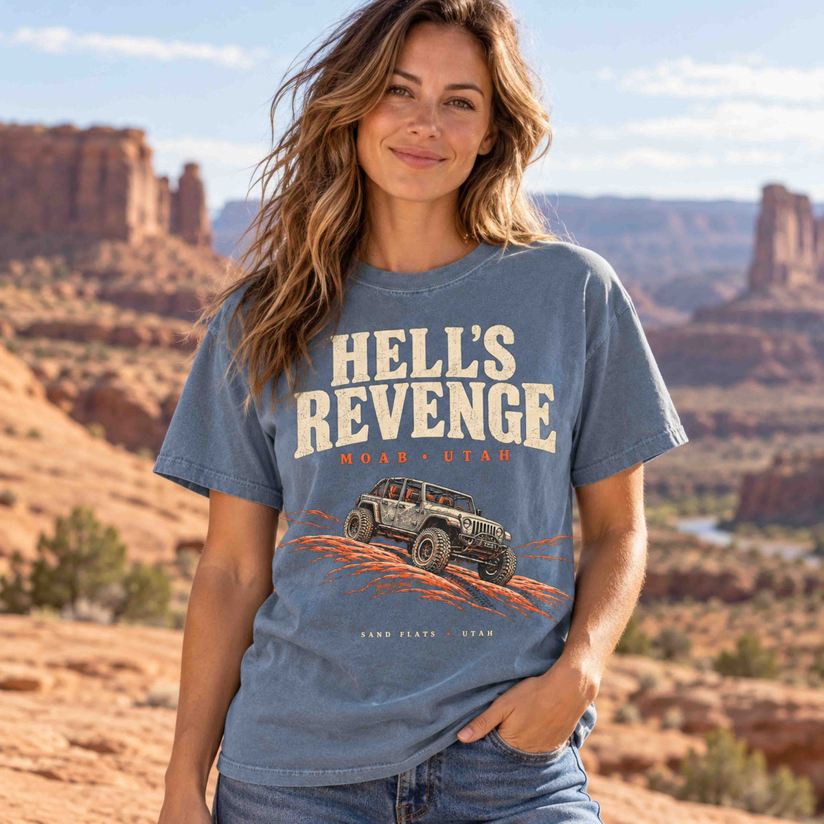 Seated man wearing a Blue Jean Hell’s Revenge Moab graphic t-shirt against a red rock desert backdrop.