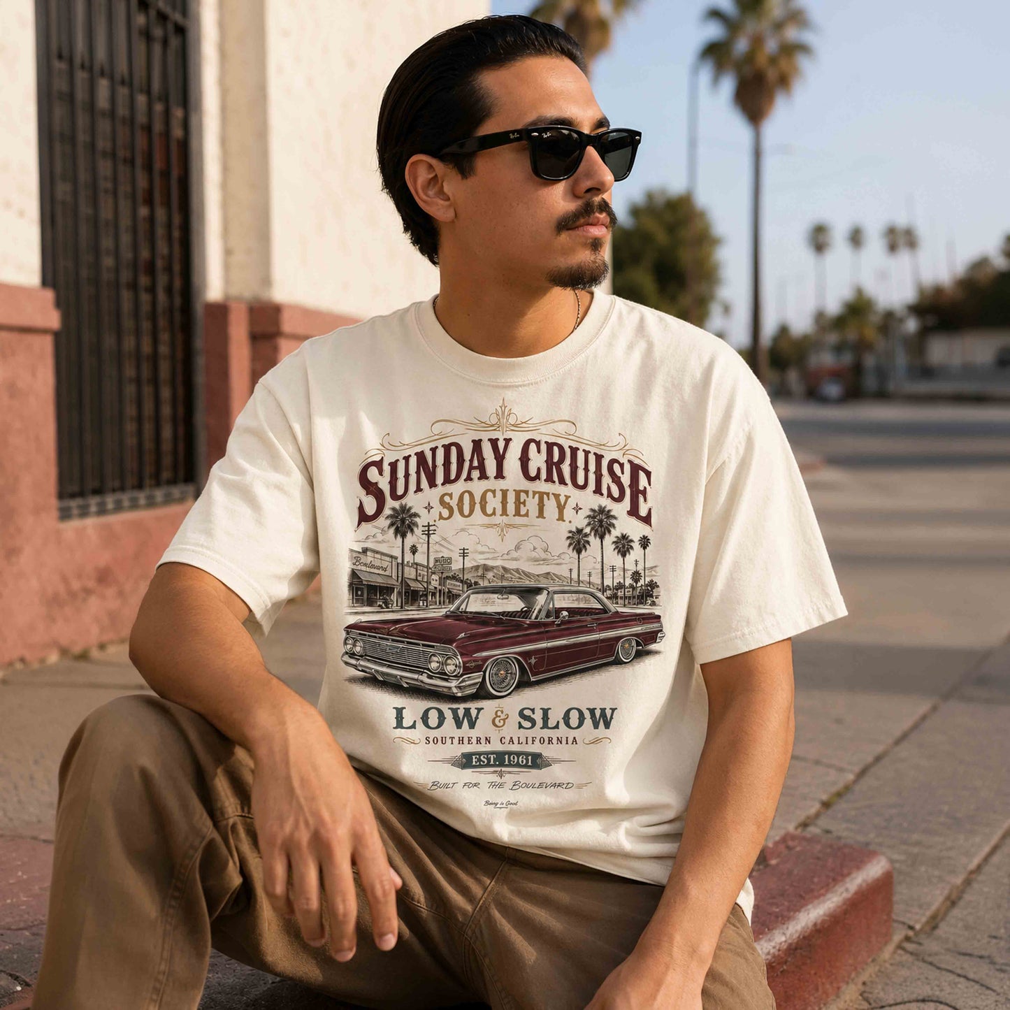 Seated man wearing a Sunday Cruise Society Southern California lowrider graphic tee