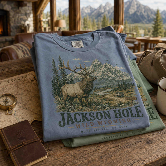 Jackson Hole Wild Wyoming graphic tees displayed outdoors with vintage Grand Teton inspired artwork