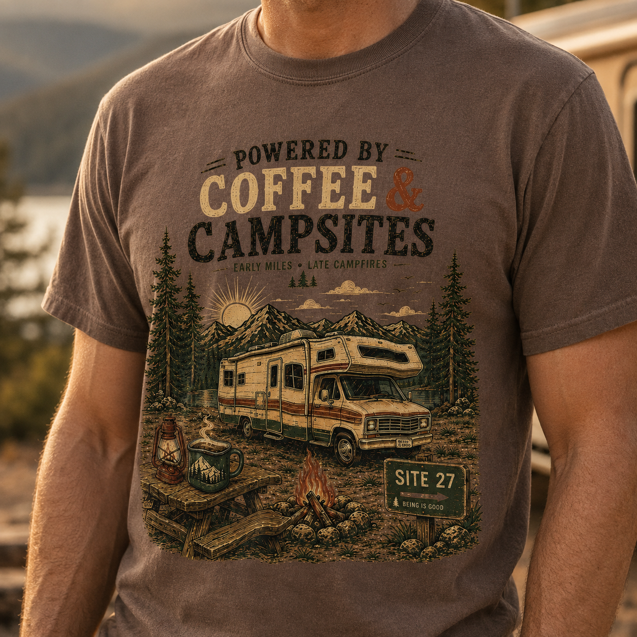 Man wearing Espresso Coffee Campsites graphic tee beside a camper at a mountain campground