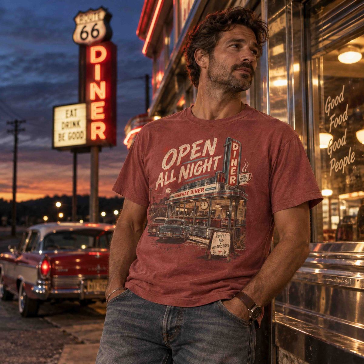 A man wearing a vintage-style graphic t-shirt leans against a diner storefront at dusk. The t-shirt is a faded reddish-brown color with a retro diner graphic and the text 'OPEN ALL NIGHT'.