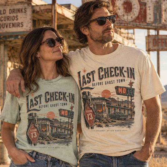 Man and woman wearing Last Check-In Motel graphic tees featuring Room 13, a vintage car and ghost town motel artwork.
