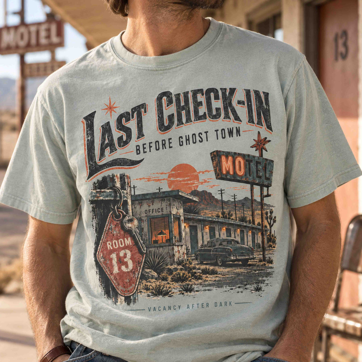 Close-up of a man wearing the light green Last Check-In Motel shirt with Room 13 ghost town artwork.