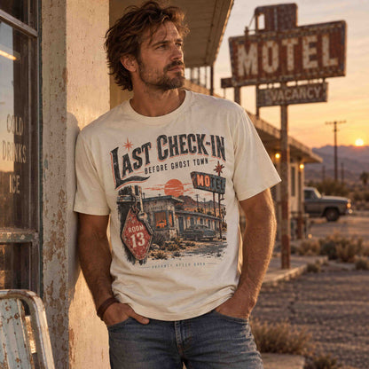 Man wearing the ivory Last Check-In Motel graphic tee at a desert roadside motel during sunset.