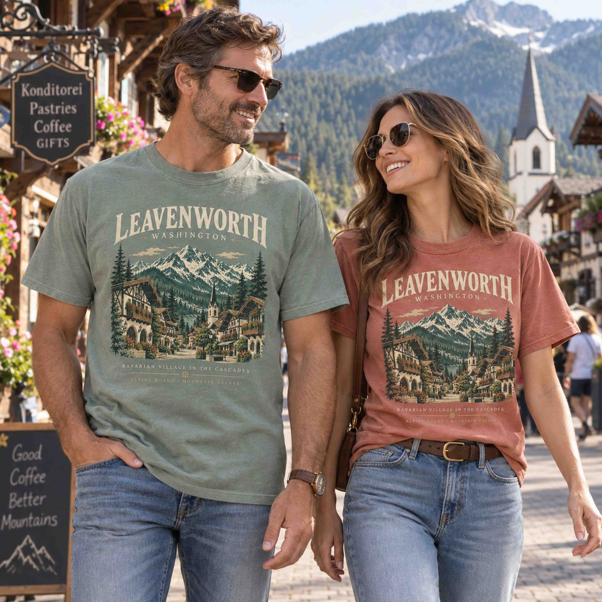 Couple walking hand in hand in Leavenworth, wearing Moss green and Yam Bavarian village and Cascade Mountains graphic tees.