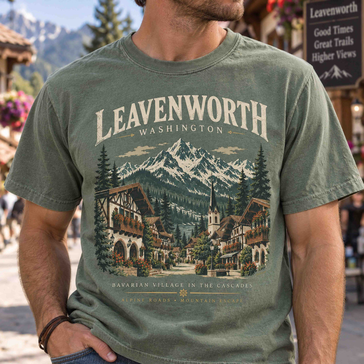 Close-up of a Moss green Leavenworth Washington tee showing Bavarian buildings, evergreen trees and Cascade Mountains artwork.