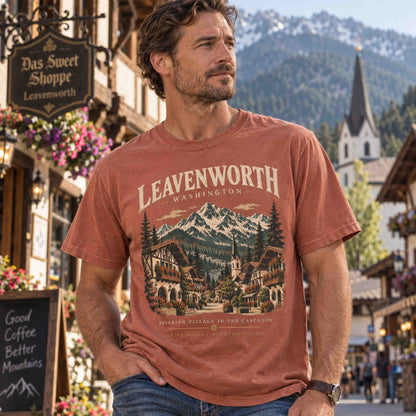 Man wearing a Yam Leavenworth Washington graphic tee featuring Bavarian village architecture and snowcapped Cascade Mountains.