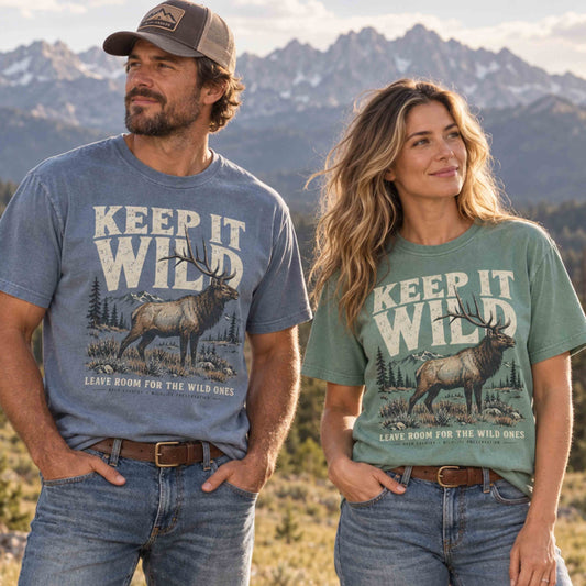 Couple wearing Keep It Wild elk wildlife graphic tees in Blue Jean and Light Green with mountains in the background