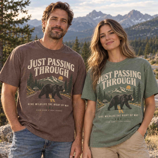 Just Passing Through Bear Wildlife Right of Way graphic tee lifestyle photo featuring Espresso and Moss shirts with a black bear crossing a mountain road.