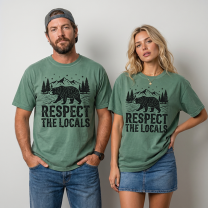 Comfort Colors graphic tee featuring a bear walking through a mountain forest scene with pine trees, stars, and “Respect The Locals” text.
