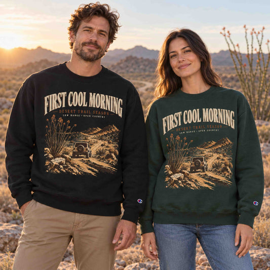 Couple wearing Black and Dark Green Champion First Cool Morning Desert Trail graphic sweatshirts in a desert sunrise setting