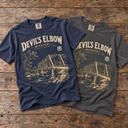 Navy and Pepper Devil's Elbow Missouri Route 66 graphic T-shirts laid together on a vintage wooden table.