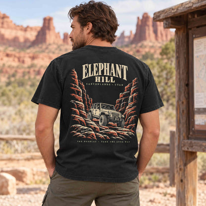 Man wearing a Black Elephant Hill tee, showing the canyon and off-road vehicle back graphic at a desert trailhead.