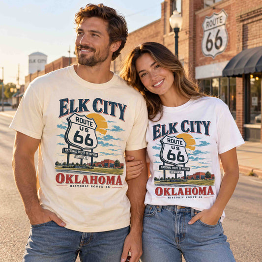 Two models wearing Being is Good Elk City Oklahoma Route 66 graphic T-shirts in Ivory and White, featuring National Route 66 Museum artwork.