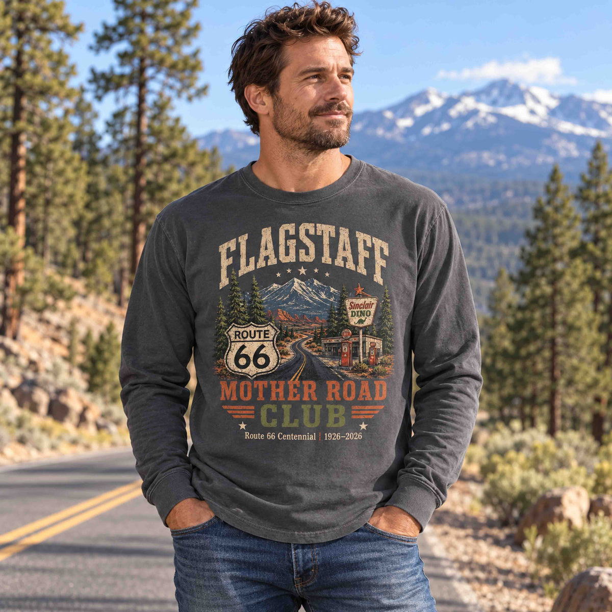 Man wearing a Pepper Flagstaff Route 66 Mother Road Club long sleeve tee beside a road, with pine trees and mountains in the background.