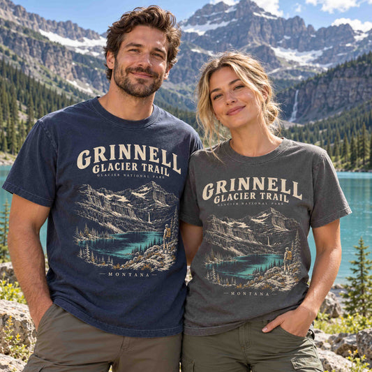 Man in Navy and woman in Pepper wearing Grinnell Glacier Trail graphic T-shirts beside a turquoise mountain lake.