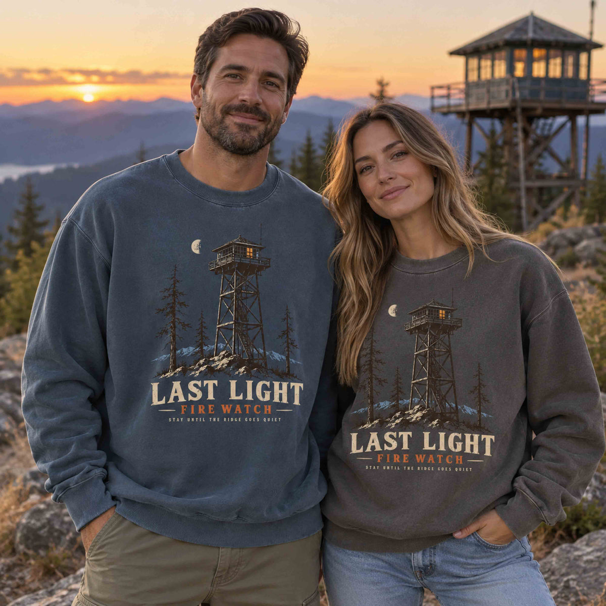 Couple wearing Denim and Pepper Last Light Fire Watch graphic sweatshirts at a mountain fire lookout during golden hour