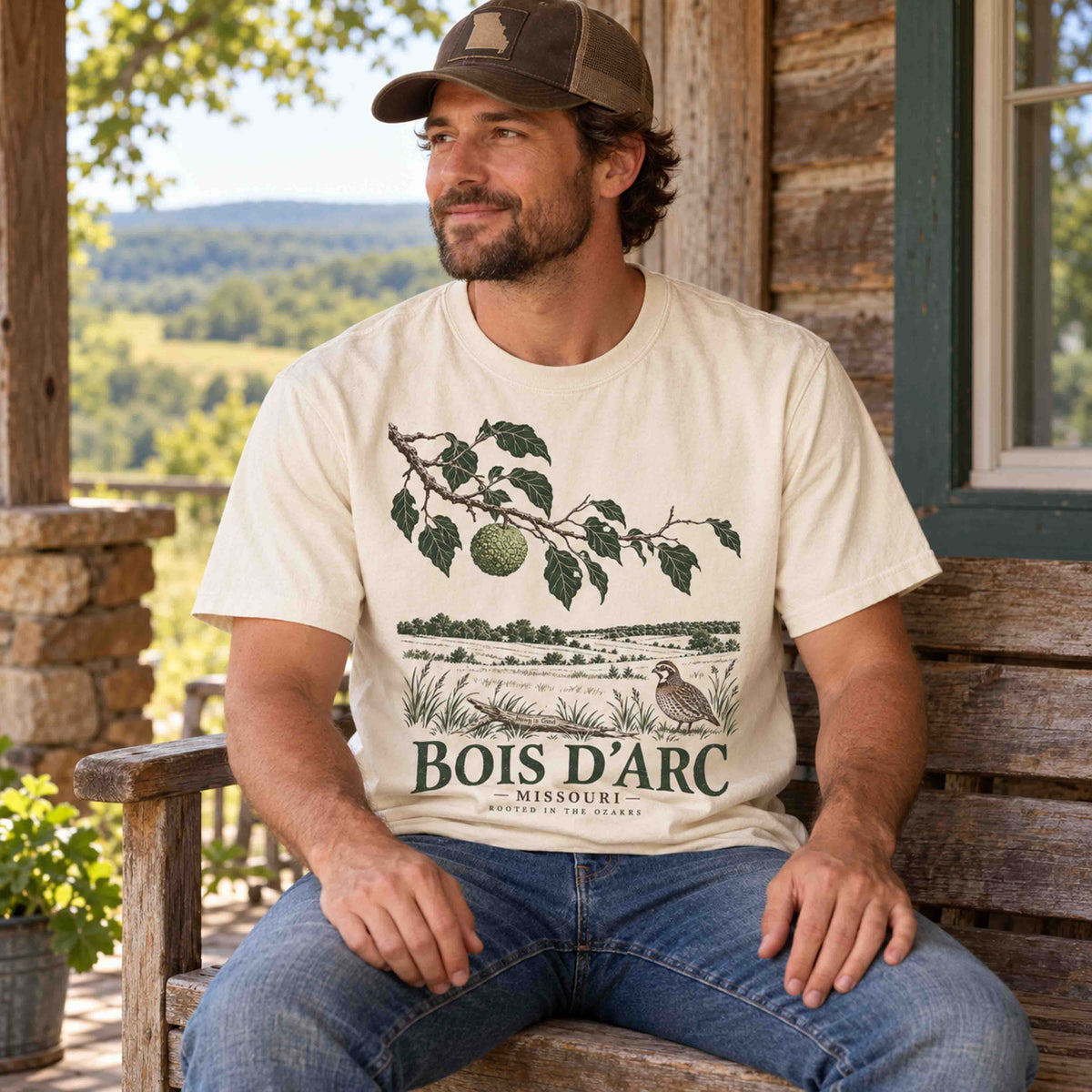 Man seated on a porch wearing an Ivory Bois D'Arc Missouri graphic T-shirt by Being is Good.