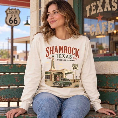 Woman seated on a green bench outside a cafe wearing an Ivory Shamrock Texas Route 66 long sleeve graphic tee.