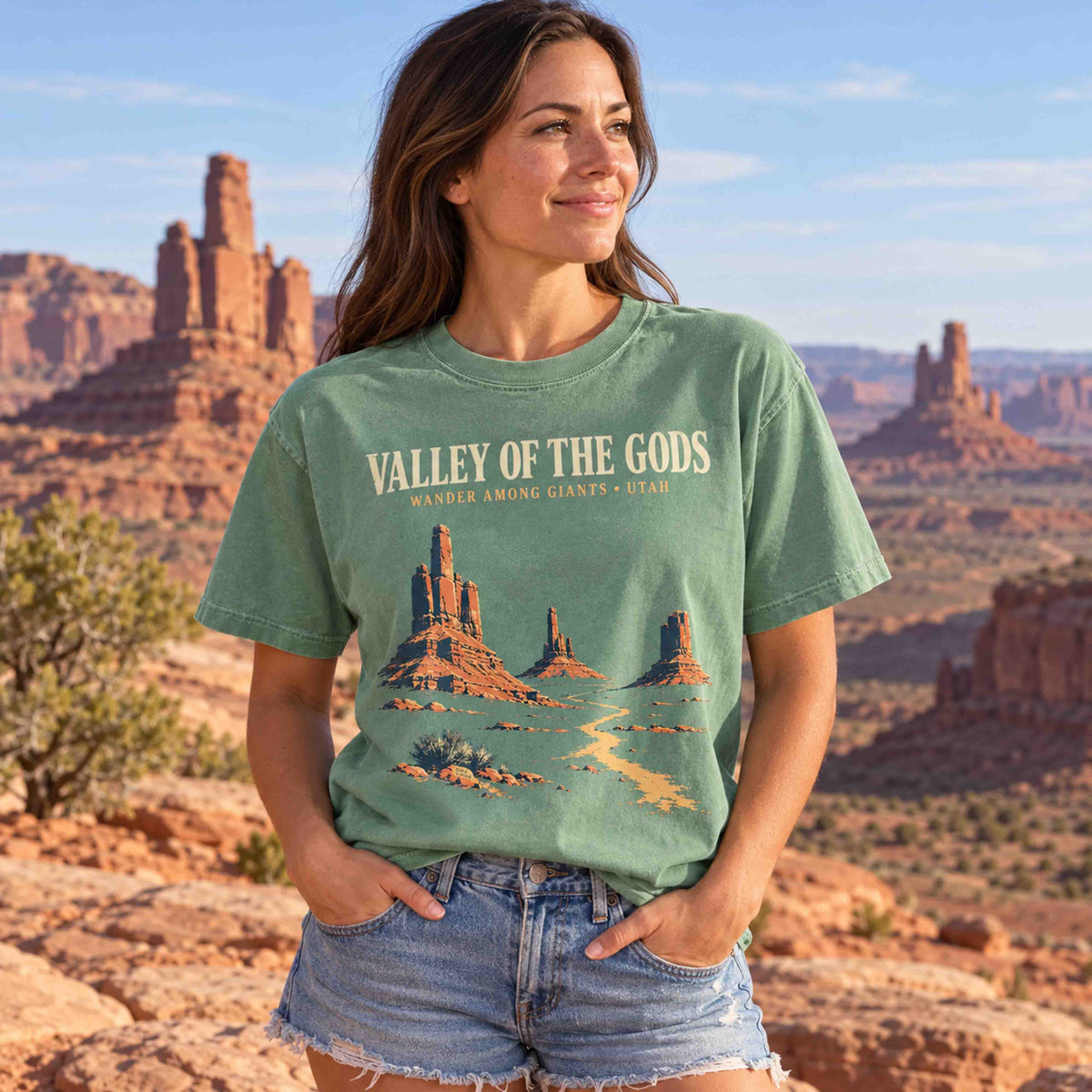 Light Green Valley of the Gods Utah graphic T-shirt laid flat on sandstone beside road trip accessories.