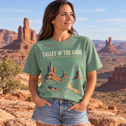 Light Green Valley of the Gods Utah graphic T-shirt laid flat on sandstone beside road trip accessories.