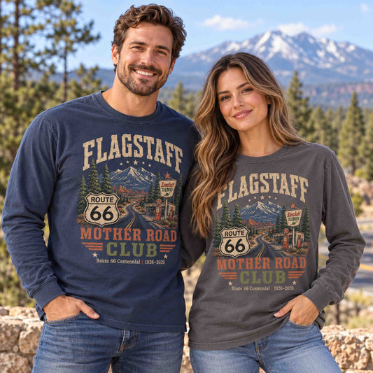 Man in Navy and woman in Pepper wearing Flagstaff Route 66 Mother Road Club long sleeve tees in a pine forest with mountains behind them.