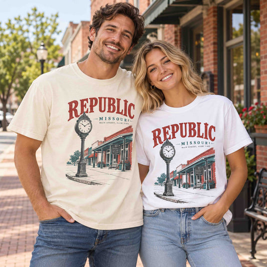 Man and woman wearing Being is Good Republic Missouri Main Street T-shirts in Ivory and White, featuring street clock and storefront artwork.