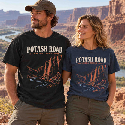 Man and woman wearing Being is Good Potash Road Moab graphic T-shirts in Black and Navy beside red rock cliffs and a river.