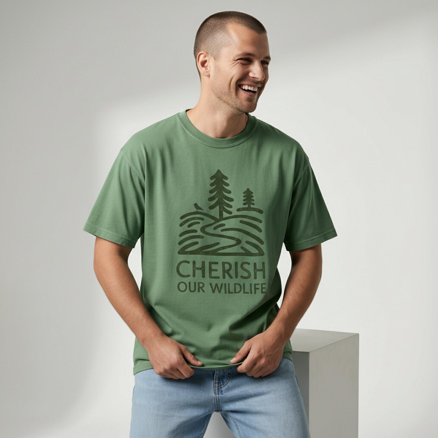 Man smiling and looking off-camera while wearing a relaxed-fit green t-shirt with a minimal vintage "Cherish Our Wildlife" tree graphic.