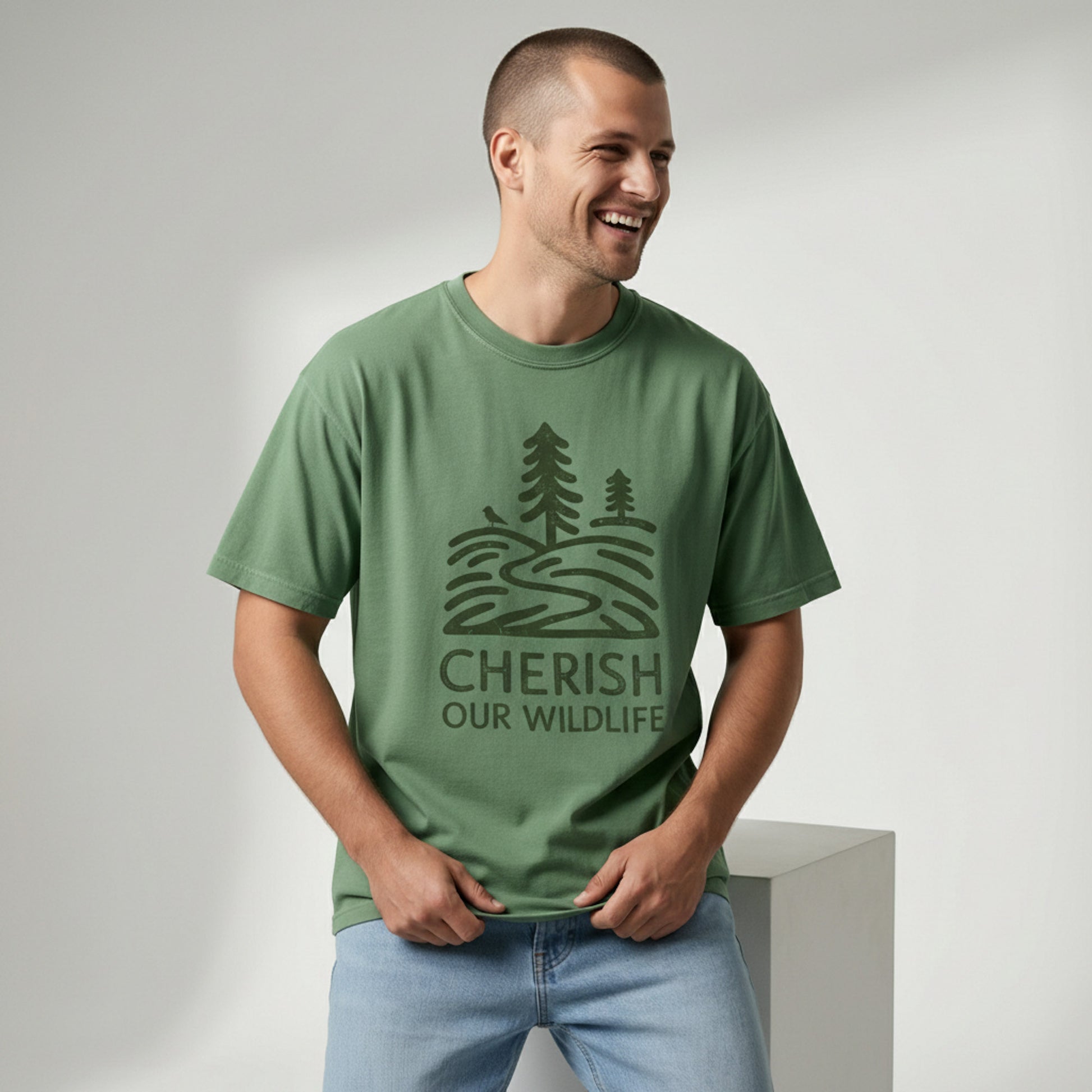 Man smiling and looking off-camera while wearing a relaxed-fit green t-shirt with a minimal vintage "Cherish Our Wildlife" tree graphic.