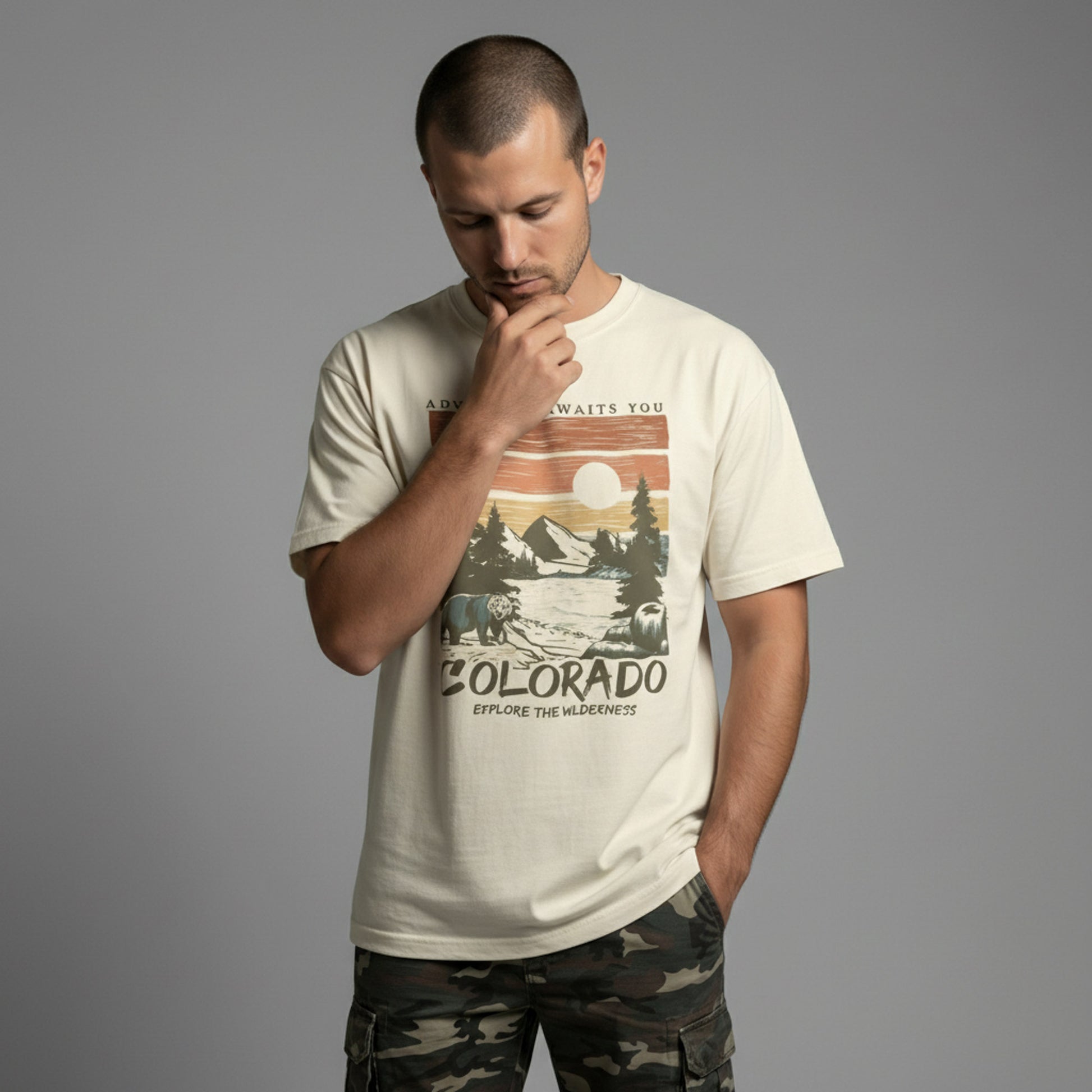 Man looking down thoughtfully while wearing a cream vintage Colorado graphic t-shirt and camo pants.