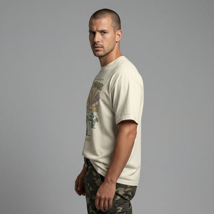 Side profile view of a man modeling a relaxed-fit cream "Explore the Wild Rockies" graphic t-shirt.
