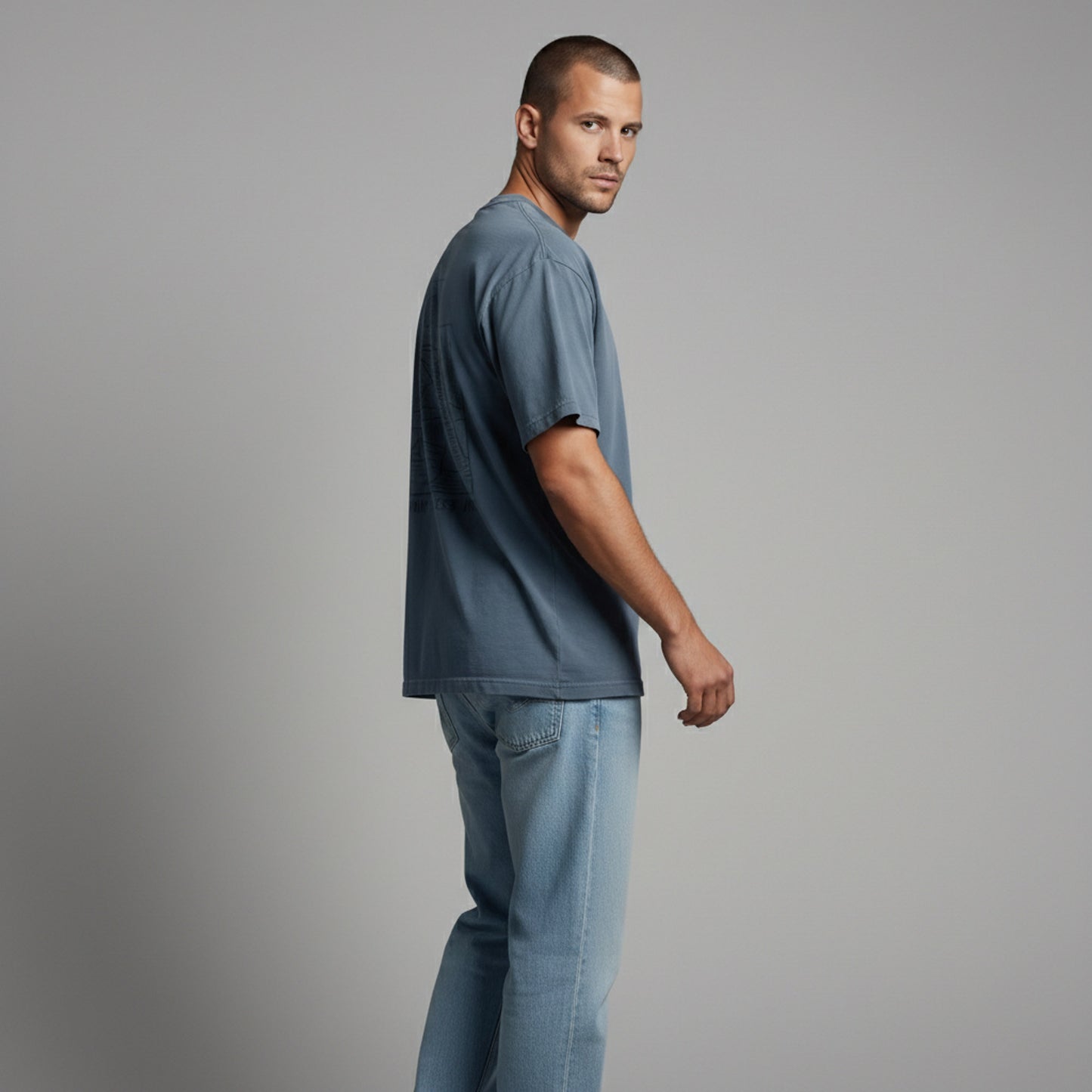Side view of a man looking back over his shoulder, wearing a dusty blue minimalist graphic tee.