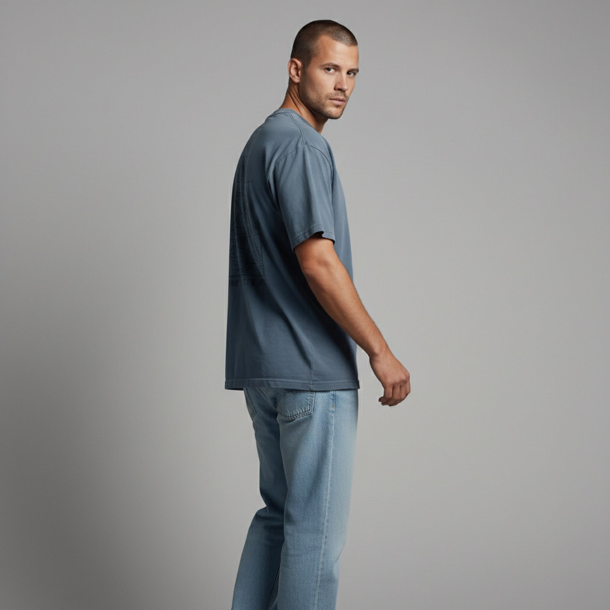 Side view of a man looking back over his shoulder, wearing a dusty blue minimalist graphic tee.