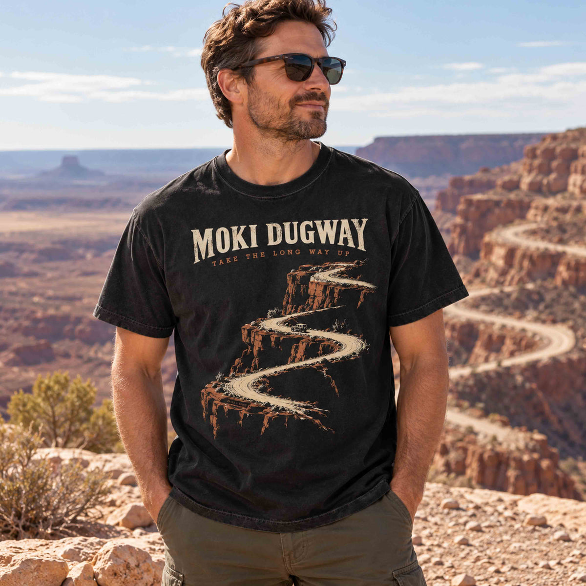 Man wearing a Black Moki Dugway scenic road trip graphic T-shirt at a Utah canyon overlook.