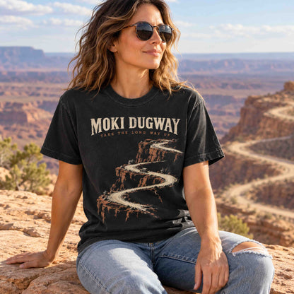 Woman wearing a Black Moki Dugway graphic tee while seated at a desert overlook.